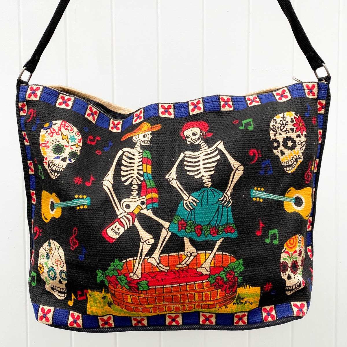 Day of the Dead Dancing Skeleton design in black, blue, red, and yellow, silkscreened on cotton handbag with black cotton strap, shown against white background.