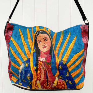 Stylized Madonna design in blues, gold and pinks, silkscreened on cotton handbag with black cotton strap, shown against white background.