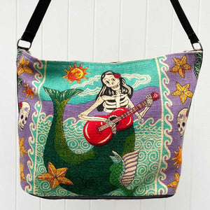 Day of the Dead Mermaid skeleton design in aqua, lavender, yellow and black, silkscreened on cotton handbag with black cotton strap, shown against white background.