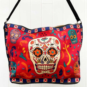 Day of the Dead skull  design in bright red, blue, yellow, and black, silkscreened on cotton handbag with black cotton strap, shown against white background.