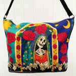 Day of the Dead female skeleton with roses, in blues, red, black and gold, silkscreened on cotton handbag with black cotton strap, shown against white background.