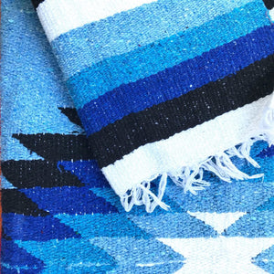 Closeup of Mexican blanket handwoven in blue, black and white diamond and stripe pattern with white fringed edge.