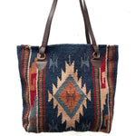 Handwoven wool handbag with center diamond design in dark blue, tan and rust with side geometric stripe design in rust, red, brown and tan, with brown strap handle, white background.