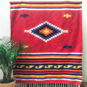 Mexican style blanket woven in diamond and stripe pattern in bright red deep blue bright yellow black and white with white fringe