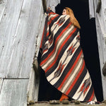 Model shown from back standing in barn doorway with handwoven Mexican blanket in earth tones draped over shoulders