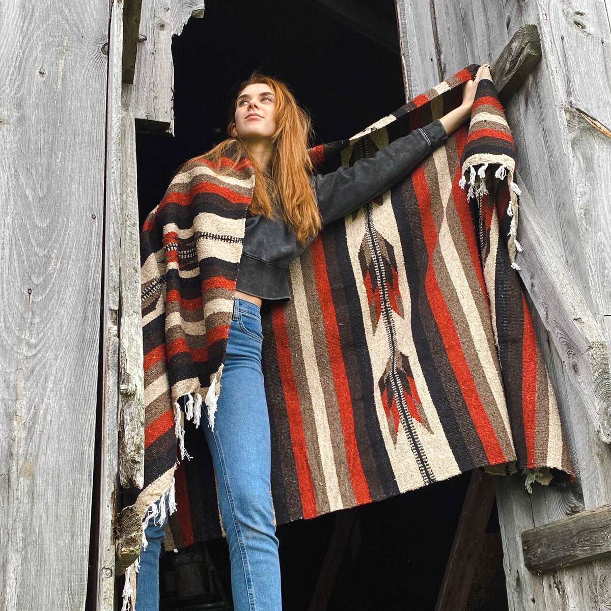 Red haired model with Mexican blanket draped over shoulder and arm Blanket is handwoven in stripe and arrow design in rust, brown and tan.