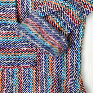 Closeup of hoodie pocket and sleeve woven in stripes of light blue, dark blue, orange, red, black and white