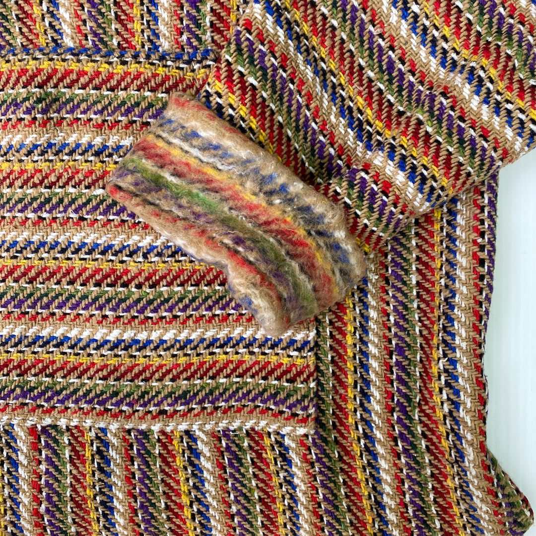 Closeup of hoodie pocket and sleeve woven in stripes of bright colors with tan and white